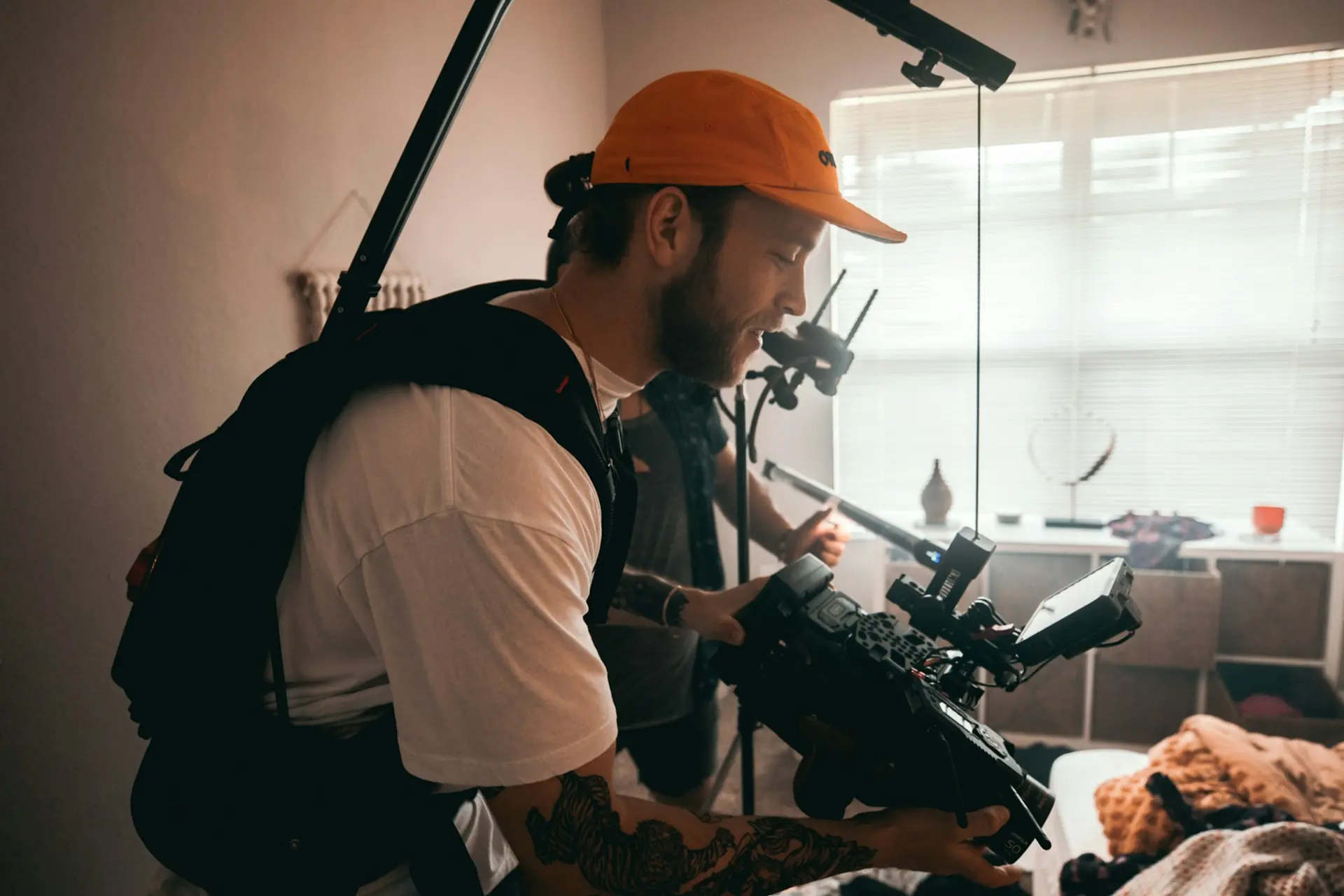 man in white shirt and orange cap holding black camera